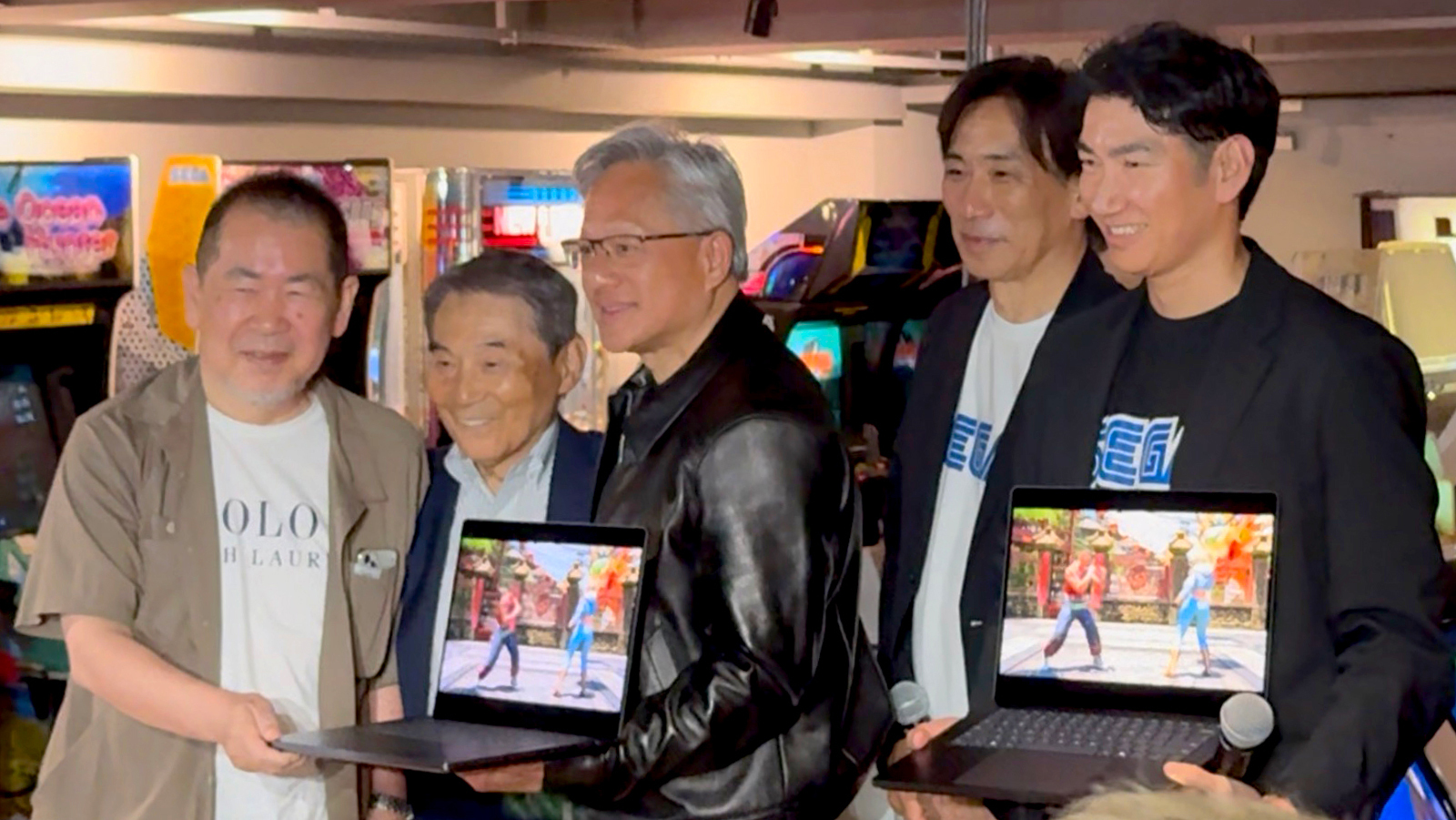 Jensen Huang holding a laptop with Shoichiro Irimajiri and Sega's team at an Akihabara arcade, July 2026